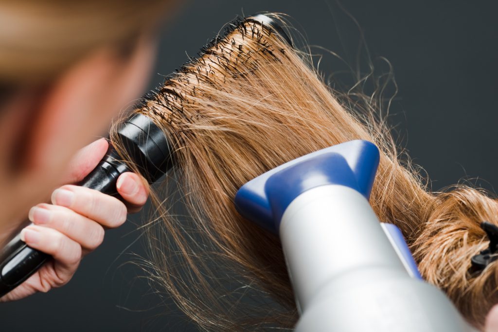 Close-up of hairdresser using hairbrush and hair-dryer